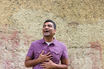 Young handsome man wearing plaid shirt standing against a cobble stone texture wall