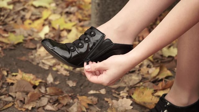 Woman relaxing in autumnal park. Female sitting on bench, putting and zipping on the black leather shoe on her feet  4K ProRes HQ codec