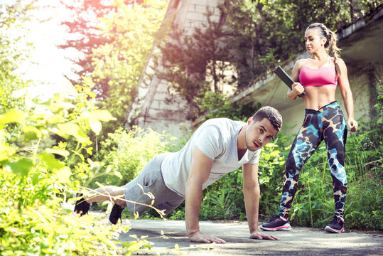 Female personal trainer and her client doing push ups outdoor