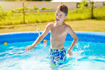 Naklejka premium Adorable young boy enjoying and cooling in backyard pool on hot summer day