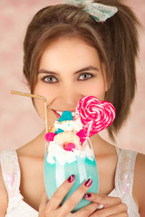 Close up of pretty cute woman holding a tasty blue milk shake with a candy heart on top, trendy clothes, studio fashion in a pink background