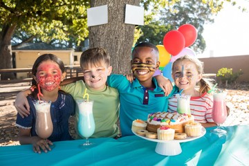 Smiling children with face paint having food and drinks at park - Powered by Adobe