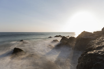 Motion blur waves breaking over rocks with setting sun at Pirates Cove in Malibu, California.