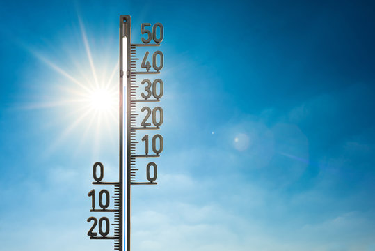 Hitzewelle, Thermometer mit Sonne und blauem Himmel im Hintergrund