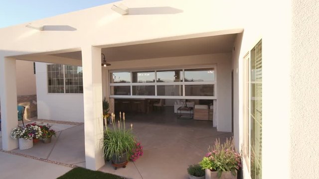 . shot lowers from white stucco exterior to backyard patio with unique garage door closing
