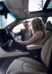 Smiling salesman talking to female customer sitting in car