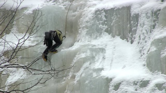 Ice climber works her way up frozen icy waterfall with ice picks and crampons