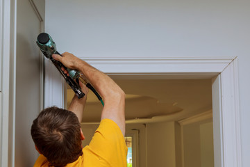 Carpenter brad using nail gun to moldings on doors, framing trim,