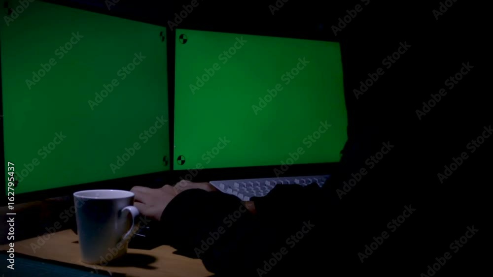 Poster hacker using computer extend green wide screen monitor with motion tracking marker in the dark room 