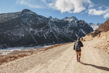 Fototapeta premium Tourists walk to black mountain with snow on the top and brown mountain with Houses and glacial trace on yellow stone ground at Thangu and Chopta valley in winter in Lachen. North Sikkim, India.