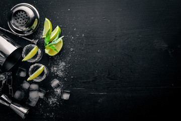 Tequila with lime and ice, on a black wooden surface. Top view. Free space. - obrazy, fototapety, plakaty