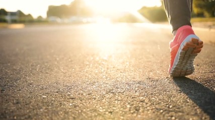 Close-up view of female feet running on an asphalt road into the sunset
