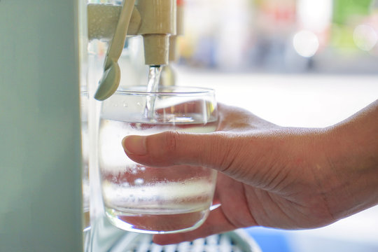 Male hand serving water of a water cooler in plastic cup.
