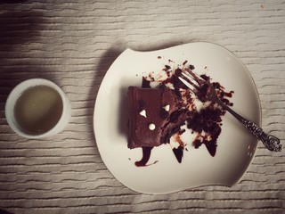 half of chocolate cake in white dish,on brown pattern table cloth,vintage design,warm light tone,blurry light background
