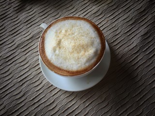 white cup of cappuccino on brown pattern table cloth,in vintage design,warm light tone,blurry light background