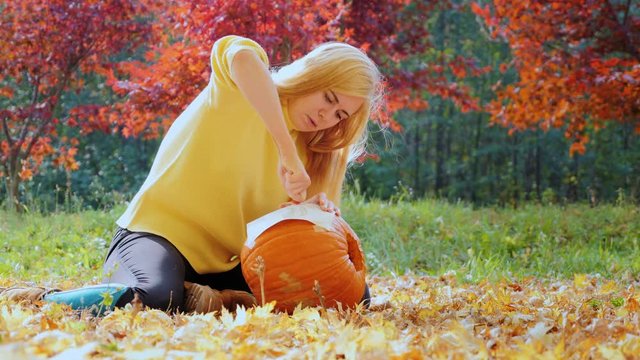 Preparing for the autumn holidays and Hellouvinu. A woman applies picture on the big pumpkin