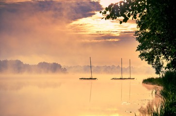 Fototapeta na wymiar Morning foggy lake landscape. Boats on the lake.