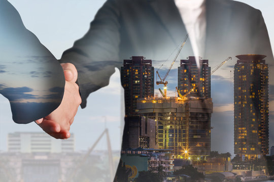 Double exposure of handshake, construction crane and building in the evening, twilight as business, commitment and industrial concept