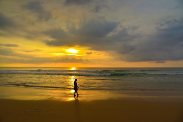 Fototapeta premium Silhouette woman walking along the beach at sunset.