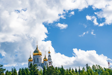 Summer landscape. Orthodox Church against the blue sky with clouds among the green pine trees