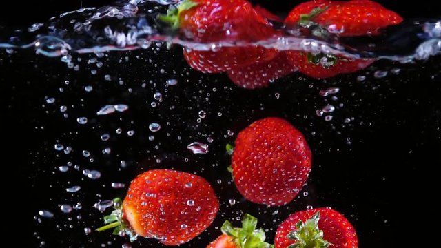 Ripe sweet strawberry dropping and swimming into the water in slow motion. Shooting with high-speed camera.
