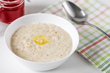 Oatmeal with a slice of butter in the white bowl on the table