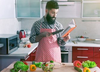 man cooking at kitchen making healthy vegetable salad and reading recipe book