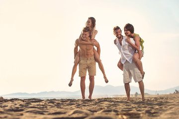 Two young men giving their girlfriends piggyback rides at the beach. Cheerful young friends enjoying summertime on the beach.