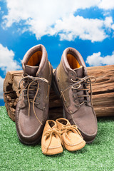 father and child shoes lean against tree stump on lush fake grass with clouds and blue sky at back, go ahead together or fathers day concept