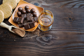 A glass of brandy. Whiskey. Assortment of chocolates on the wooden surface. Top view
