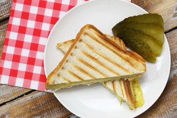 Two pieces of toasts with melted cheese with gherkin on the side
