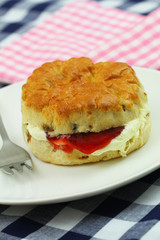 Traditional English scone with strawberry jam and fresh clotted cream on white plate, closeup
