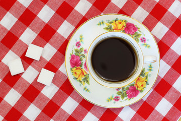 Black tea in vintage porcelain cup, sugar cubes on red and white checkered cloth
