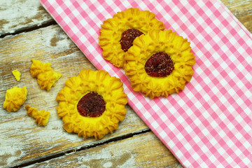Crunchy cookies with strawberry jam on pink cloth and wooden surface
