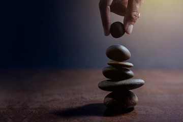 Balance-Konzept zwischen Leben und Arbeit, die von Hand präsentiert werden und einen natürlichen Zen-Felsstein auf Stapel, Seitenansicht und dunklem Licht setzen