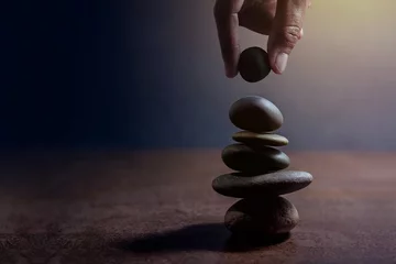 Selbstklebende Fototapete Zen Balance-Konzept zwischen Leben und Arbeit, die von Hand präsentiert werden und einen natürlichen Zen-Felsstein auf Stapel, Seitenansicht und dunklem Licht setzen