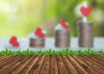 Empty wooden deck table and grass with heart on coins tower with nature background.