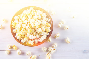 Salty popcorn in a wooden cup is on a white table. Popcorn lies around the bowl. Top view.