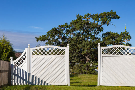 White garden wooden fence and gates to yard with green grass and trees