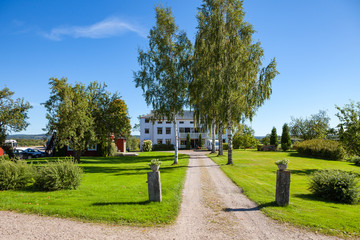 Farm house and road to it. White wooden cottage with trees. Hedemora, Sweden