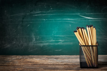 Many pencils in the metal holder on wooden table on green board background