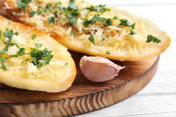 Tasty bread slices with garlic, cheese and herbs on wooden cutting board