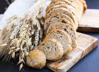 Whole wheat bread with wheat ears and seeds , bread slices on wooden board