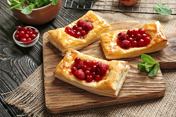 Delicious pastries with berries and honey on cutting board