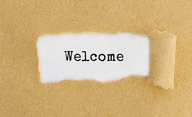Text Welcome appearing behind ripped brown paper