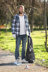 Young handsome volunteer picking up litter in park