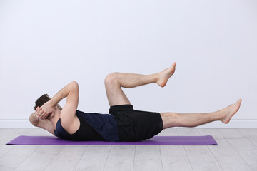 Young man doing bicycle crunch exercise on white wall background