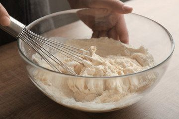 Human hands stirring dough with flour in glass bowl on table