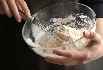 Human hands stirring dough with flour in glass bowl
