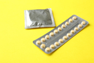 Birth pills and condom on yellow background